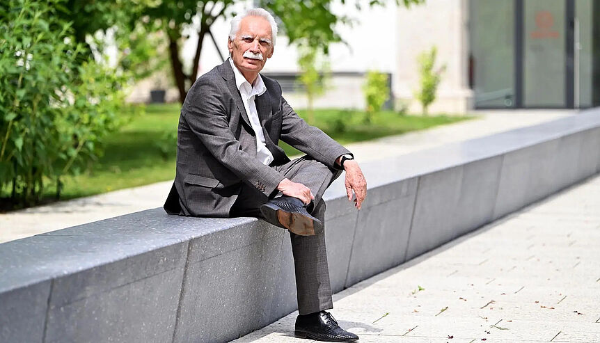 Karl Sigmund sitzend auf einer steinernen Bank (Hintergrund: Wiese mit Strauch und Baum)